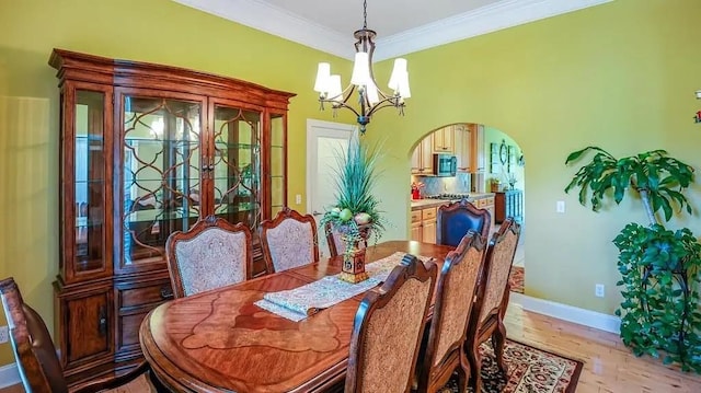 dining area with arched walkways, light wood-style flooring, ornamental molding, a chandelier, and baseboards