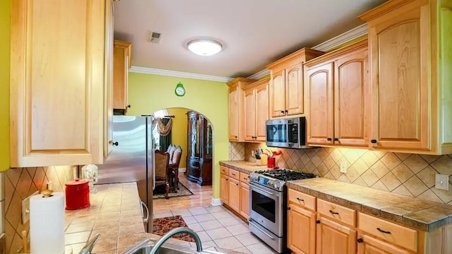 kitchen featuring arched walkways, stainless steel appliances, ornamental molding, tile counters, and tasteful backsplash