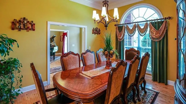 dining space with light wood-style floors, baseboards, ornamental molding, and a notable chandelier