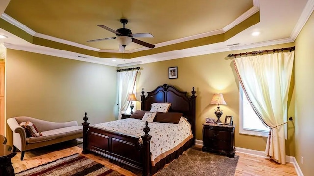 bedroom with baseboards, ceiling fan, wood finished floors, a tray ceiling, and crown molding