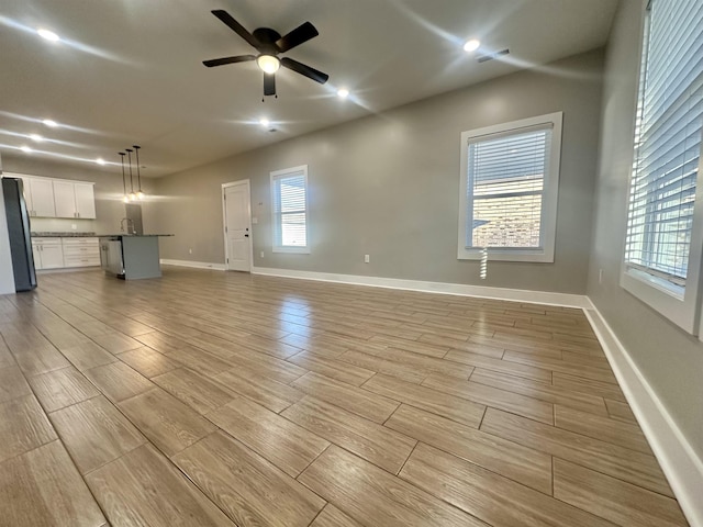 unfurnished living room featuring ceiling fan, wood finish floors, baseboards, and a healthy amount of sunlight