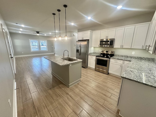 kitchen with light stone counters, appliances with stainless steel finishes, white cabinetry, a sink, and an island with sink