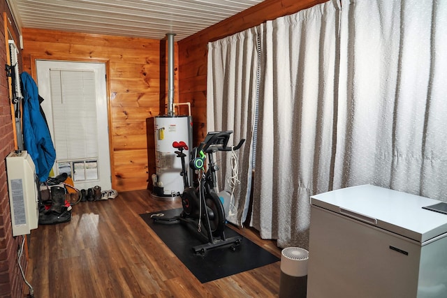 exercise room with dark wood-type flooring, gas water heater, wooden walls, and heating unit