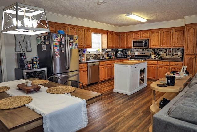 kitchen with stainless steel appliances, dark countertops, hanging light fixtures, brown cabinetry, and a kitchen island