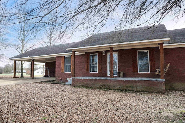 ranch-style home with an attached carport, covered porch, brick siding, a shingled roof, and driveway