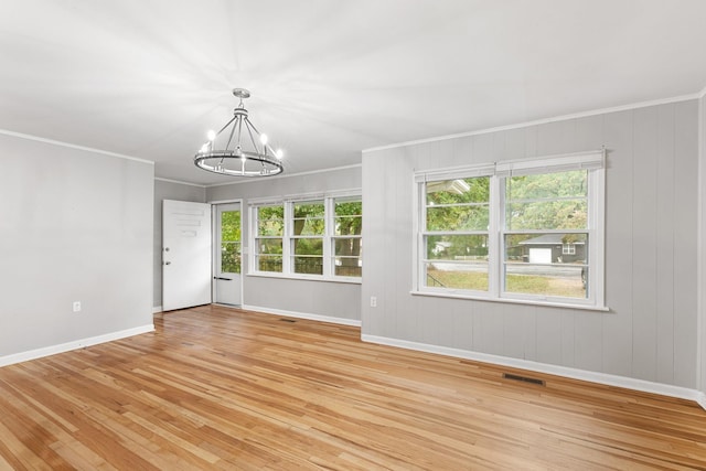 unfurnished room with ornamental molding, a healthy amount of sunlight, light wood-type flooring, and an inviting chandelier