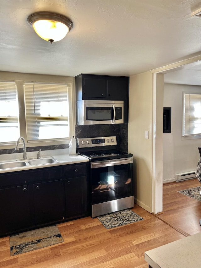 kitchen featuring light wood-type flooring, sink, appliances with stainless steel finishes, and a baseboard radiator