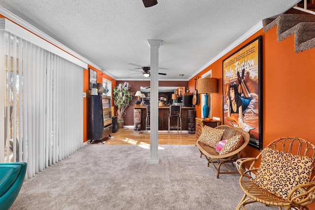 sitting room featuring carpet, ornamental molding, a textured ceiling, and decorative columns