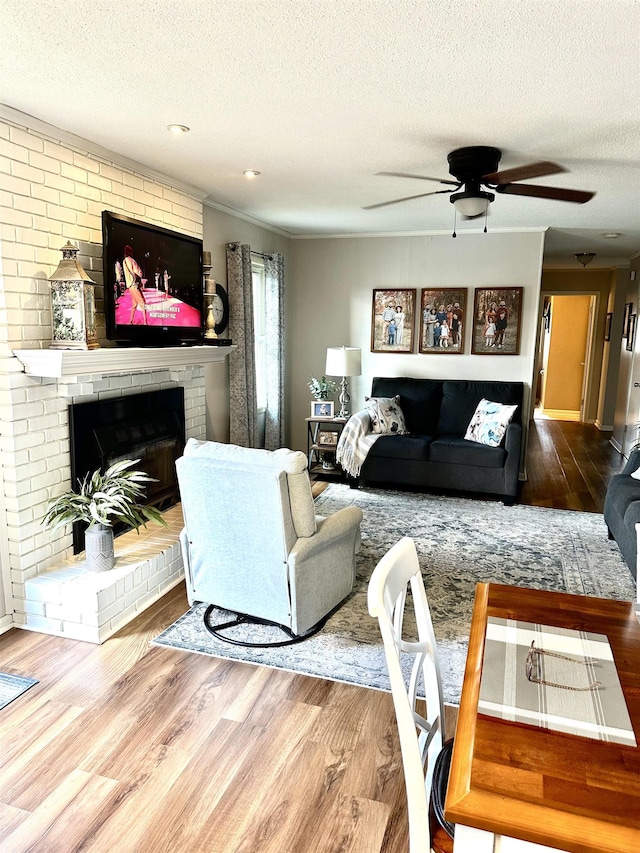  - living area with a textured ceiling, a ceiling fan, wood finished floors, and a brick fireplace