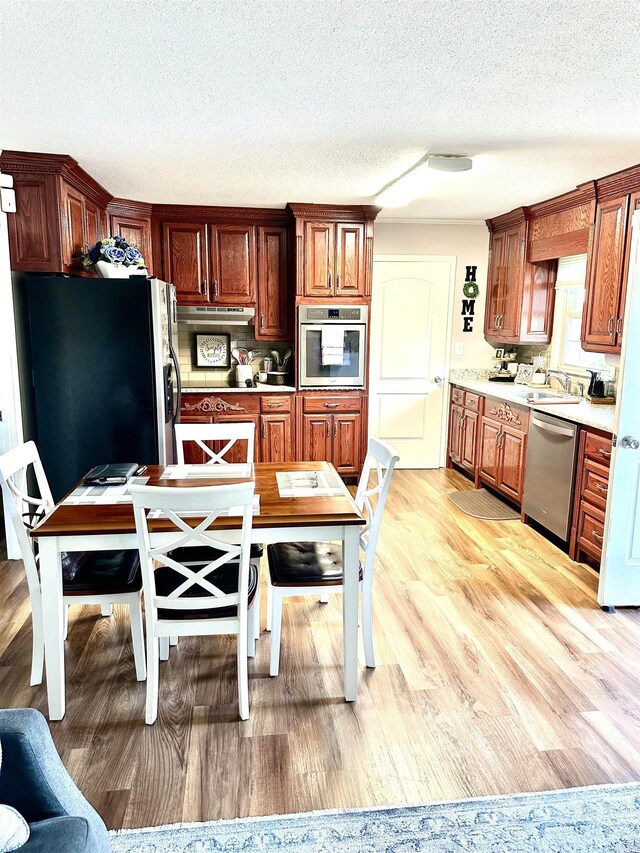  - kitchen featuring stainless steel appliances, a textured ceiling, light wood-style flooring, light countertops, and a sink