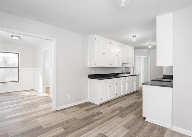 kitchen with dark countertops, baseboards, light wood-type flooring, white cabinets, and a sink