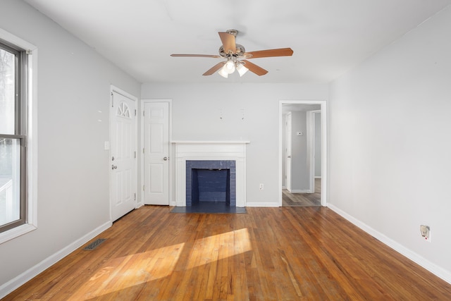 unfurnished living room with visible vents, wood finished floors, baseboards, a brick fireplace, and ceiling fan