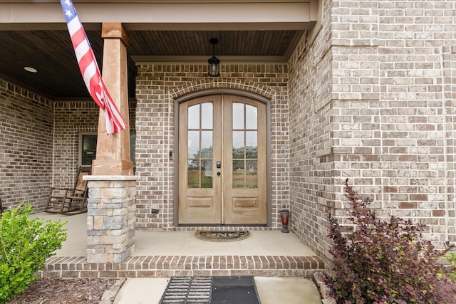 doorway to property with french doors, brick siding, and covered porch