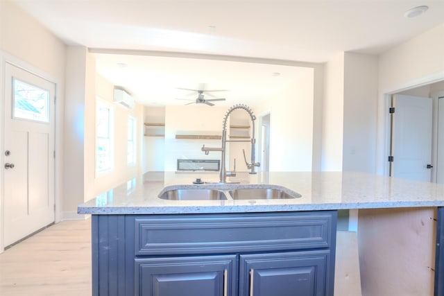  - kitchen with blue cabinets, light wood-type flooring, a wall mounted AC, an island with sink, and light stone countertops