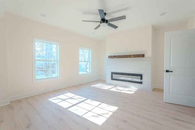  - unfurnished living room featuring light wood-type flooring, a glass covered fireplace, and a ceiling fan