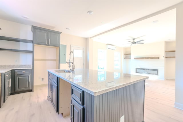  - kitchen with open shelves, light wood-style flooring, ceiling fan, light stone counters, and a center island with sink
