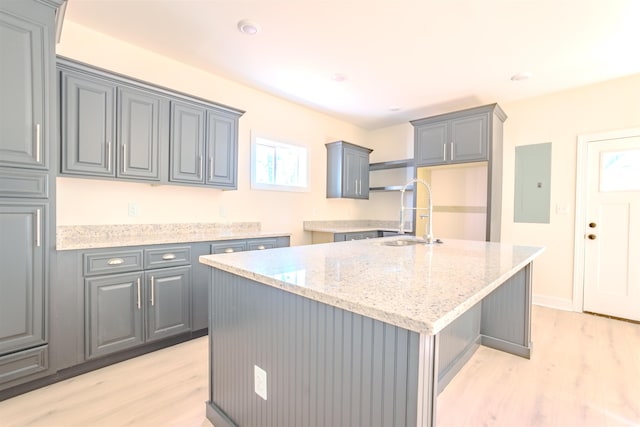  - kitchen with light wood finished floors, gray cabinets, electric panel, and light stone countertops