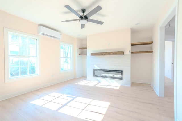  - unfurnished living room featuring a wall mounted air conditioner, light wood-style flooring, a glass covered fireplace, and ceiling fan