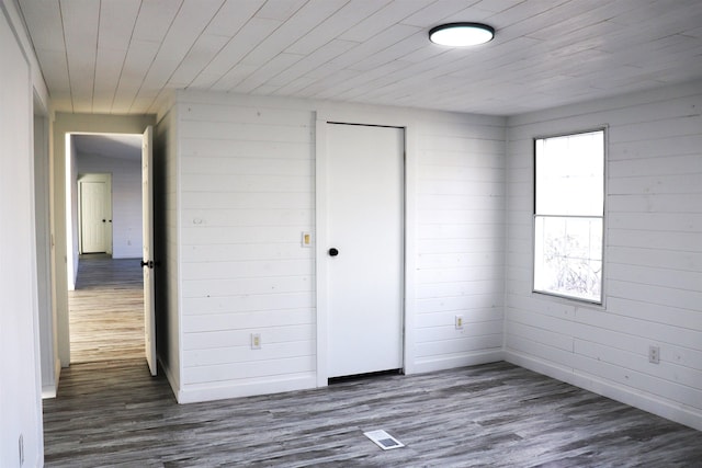 unfurnished room with wooden ceiling, visible vents, wood finished floors, and wood walls