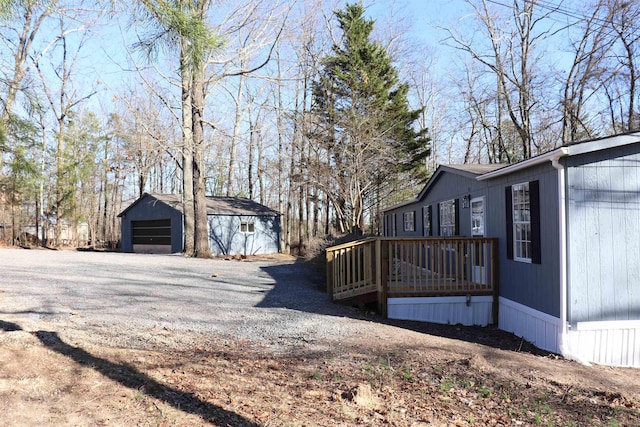 view of side of property featuring gravel driveway, a detached garage, a deck, and an outdoor structure