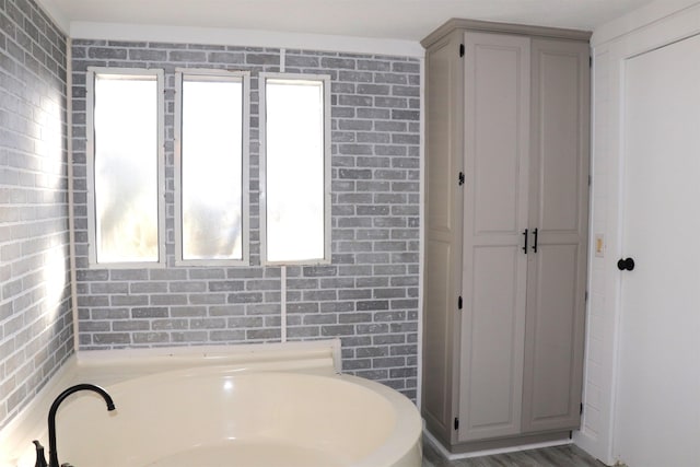 bathroom featuring brick wall and a bath