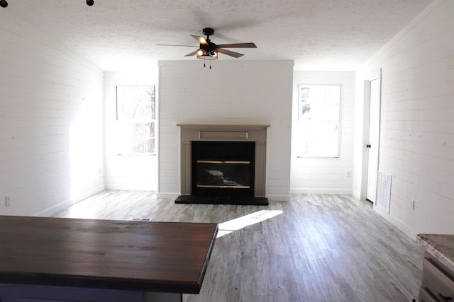 unfurnished living room featuring a ceiling fan, a glass covered fireplace, a textured ceiling, and wood finished floors