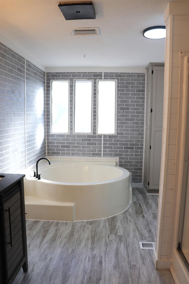 full bath with a textured ceiling, wood finished floors, vanity, visible vents, and a bath