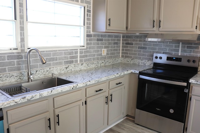 kitchen featuring range hood, electric stove, a sink, and backsplash