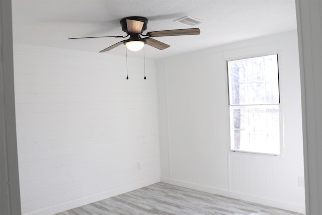 spare room featuring a healthy amount of sunlight, light wood finished floors, ceiling fan, and visible vents