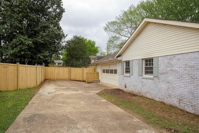 view of side of property with driveway, a garage, fence, and brick siding