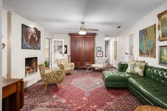 living room with ceiling fan, a fireplace, a textured ceiling, ornamental molding, and visible vents