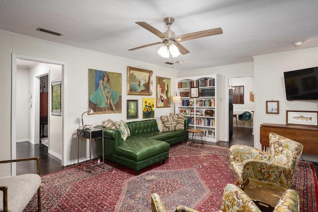 living room with visible vents, a ceiling fan, a textured ceiling, crown molding, and wood finished floors