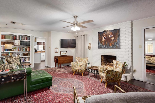 living room with a textured ceiling, a ceiling fan, crown molding, a brick fireplace, and visible vents