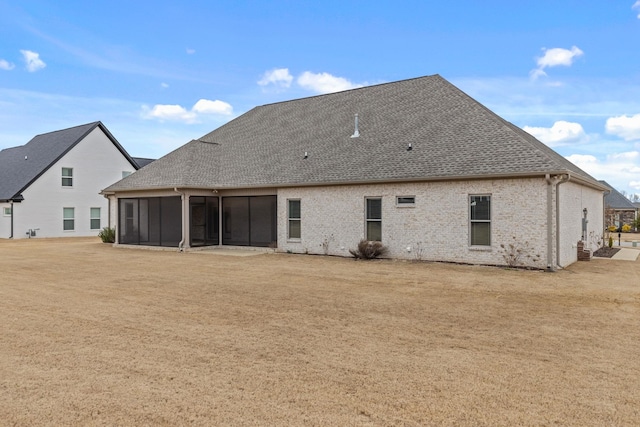 back of house featuring brick siding, a sunroom, and a shingled roof