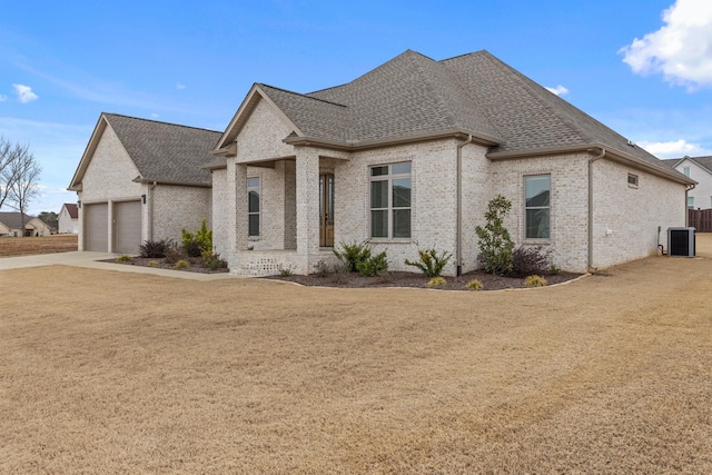 view of front of house featuring brick siding, a front lawn, central AC, roof with shingles, and an attached garage