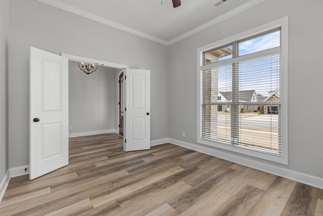 unfurnished room with ceiling fan with notable chandelier, wood finished floors, baseboards, and ornamental molding