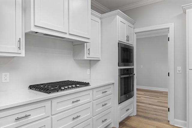 kitchen featuring light wood finished floors, ornamental molding, white cabinets, and stainless steel gas stovetop