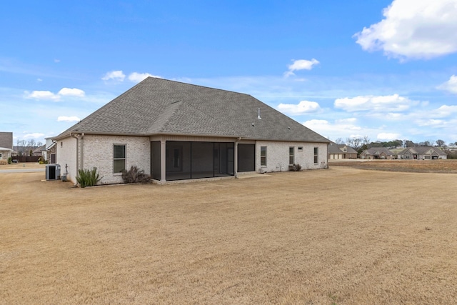 back of property with a sunroom, central AC, a yard, a shingled roof, and brick siding