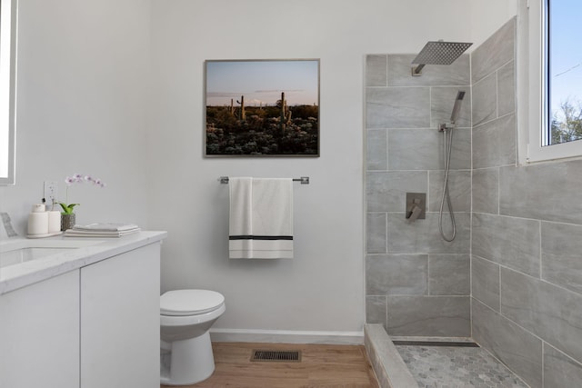  - bathroom featuring a tile shower, toilet, vanity, baseboards, and wood finished floors