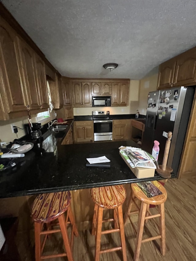 kitchen featuring stainless steel electric range oven, refrigerator with ice dispenser, black microwave, a peninsula, and a kitchen breakfast bar