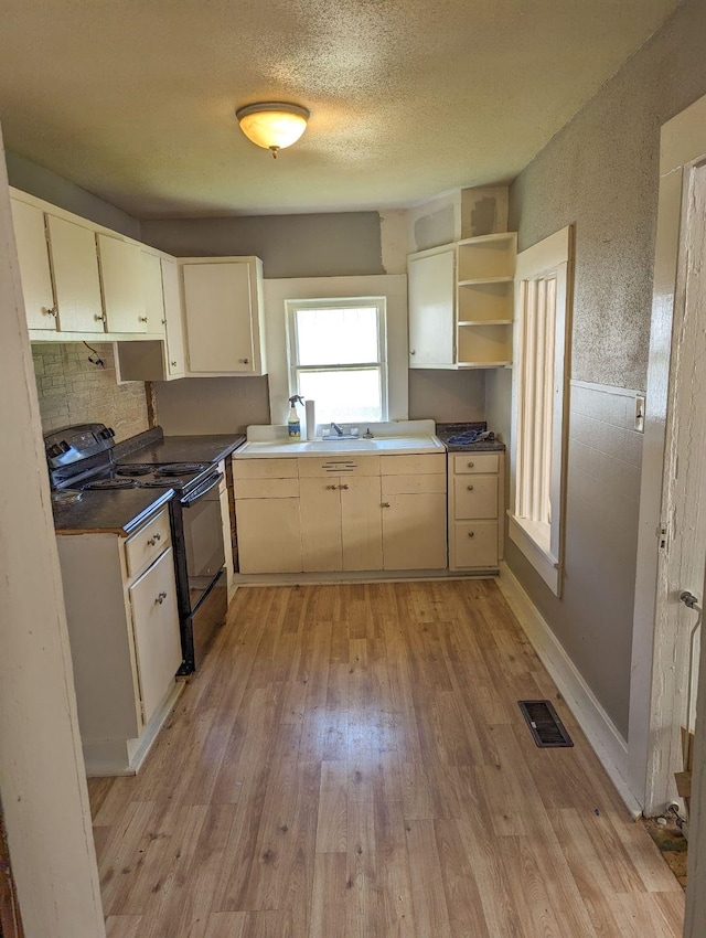  - kitchen featuring black / electric stove, light wood-style flooring, open shelves, dark countertops, and a textured ceiling