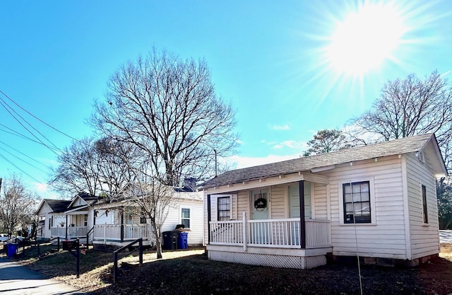 view of front facade featuring covered porch, roof with shingles, and fence