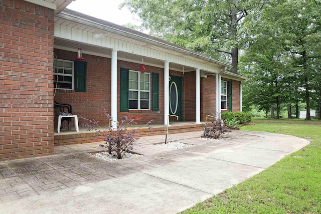  - view of exterior entry with a porch, brick siding, and a lawn