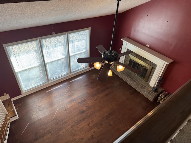 unfurnished dining area with a ceiling fan, a glass covered fireplace, dark wood finished floors, and a textured ceiling