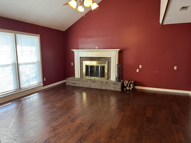 unfurnished living room with lofted ceiling, a textured ceiling, wood finished floors, baseboards, and a brick fireplace