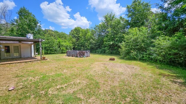  - view of grassy yard with french doors, an outdoor fire pit, an outdoor pool, a wooden deck, and a wooded view