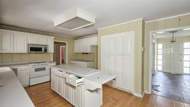  - kitchen with stainless steel microwave, white range oven, a kitchen island, ornamental molding, and light wood-style flooring