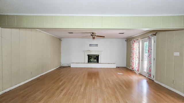  - unfurnished living room featuring light wood-style floors, a ceiling fan, a fireplace with raised hearth, and wood walls