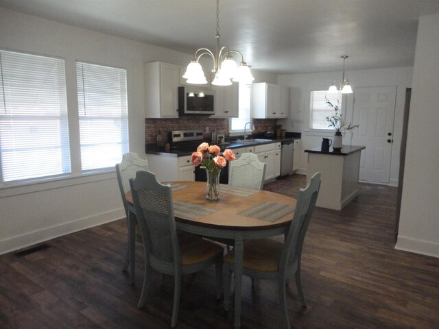 kitchen featuring pendant lighting, dark wood-type flooring, white cabinets, appliances with stainless steel finishes, and a notable chandelier