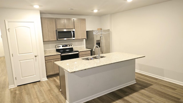 kitchen featuring a center island with sink, sink, light hardwood / wood-style flooring, light stone countertops, and appliances with stainless steel finishes